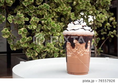 Mocha  frappe in plastic cup with whipping cream and chocolate sauce topping. 76557926