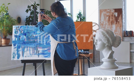 A woman paint artist taking pictures of her abstract oil painting on her phone A woman paint artist taking pictures of her abstract oil painting on her phone 76558453