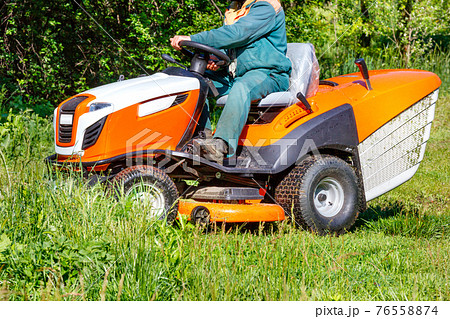 A gardener mows a green meadow with a tractor lawn mower. 76558874