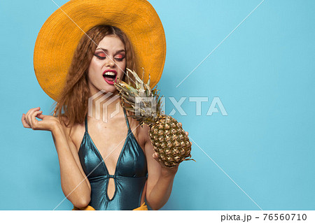 Woman in swimsuit hat exotic fruits summer fun blue background Woman in swimsuit hat exotic fruits summer fun blue background 76560710