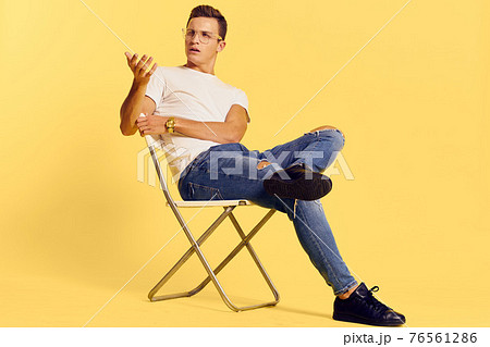 Cute man sitting on a chair white t-shirt jeans lifestyle modern style yellow background 76561286