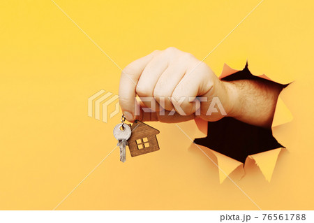 Male hand with house keys through a hole in yellow paper wall. House sale and rent concept 76561788
