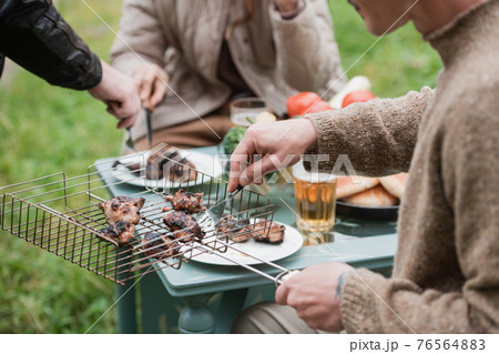 A man serves delicious grilled meat to his girlfriend on the picnic table. Outdoor recreation on a warm autumn day. Dinner together on the street. A man serves delicious grilled meat to his girlfriend on the picnic table. Outdoor recreation on a warm autumn day. Dinner together on the street. 76564883