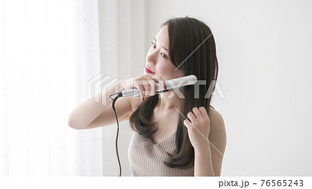 ヘアアイロンで髪の毛をストレートにする若い女性の写真素材