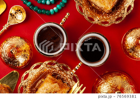 Turkish baklava and coffee in oriental dishware on red background Turkish baklava and coffee in oriental dishware on red background 76569381