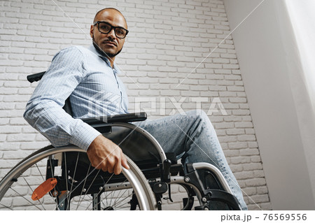 African american man in wheelchair sitting near the window alone at home African american man in wheelchair sitting near the window alone at home 76569556