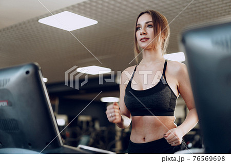 Pretty fit woman in black sportrswear training on a treadmill 76569698