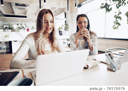 Two young female colleagues discussing business project together in office Two young female colleagues discussing business project together in office 76570079