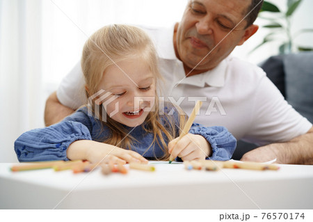 Grandfather and granddaughter drawing together in living room 76570174