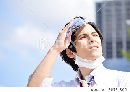 暑くてマスクを外してハンカチで汗を拭いている若い男性 76574306
