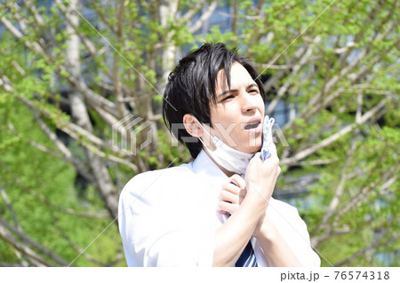 暑くてマスクを外してハンカチで汗を拭いている若い男性 暑くてマスクを外してハンカチで汗を拭いている若い男性 76574318