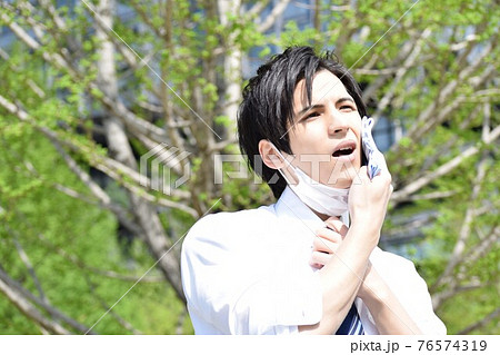 暑くてマスクを外してハンカチで汗を拭いている若い男性 76574319
