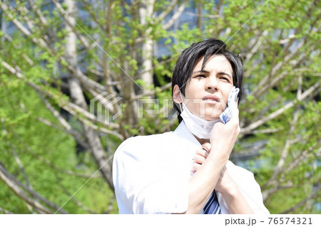 暑くてマスクを外してハンカチで汗を拭いている若い男性 76574321