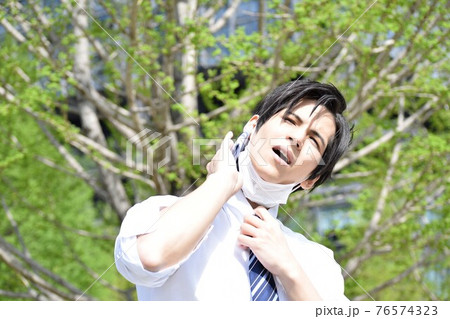 暑くてマスクを外してハンカチで汗を拭いている若い男性 76574323