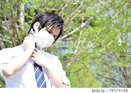 マスクの息苦しさでハンカチで汗を拭いている若い男性 76574708