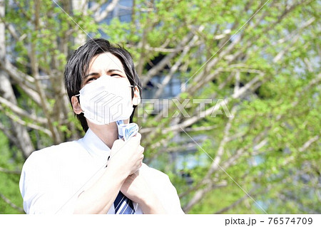 マスクの息苦しさでハンカチで汗を拭いている若い男性 76574709