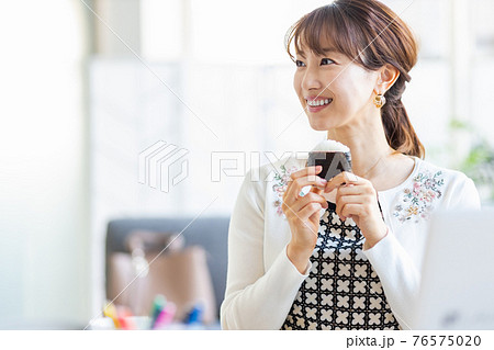 明るい室内でおにぎりを食べる女性 76575020