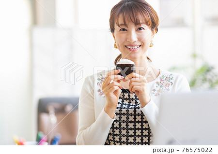 明るい室内でおにぎりを食べる女性 76575022