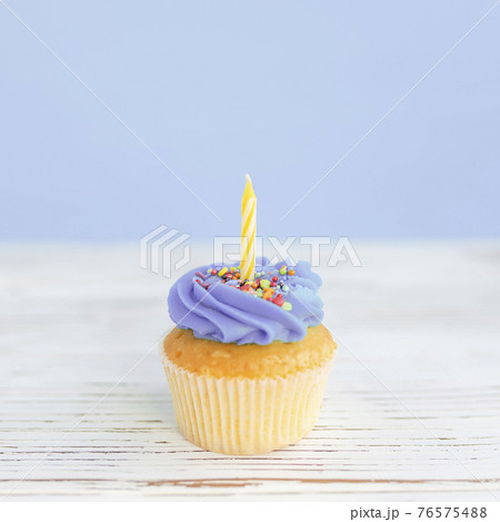 Birthday greeting concept. Yellow candle on muffin, cupcake. Blue background Birthday greeting concept. Yellow candle on muffin, cupcake. Blue background 76575488