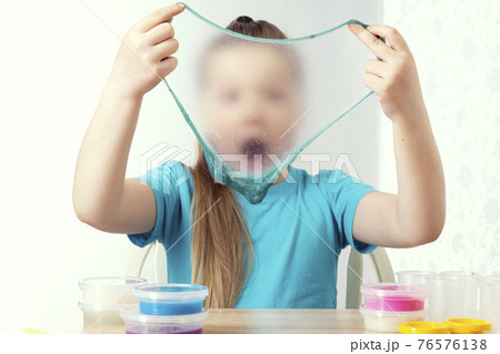 A blonde child is playing with a slime. Little beautiful caucasian girl is playing with many slimes. Play Slime Toy 76576138