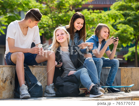 Portrait of four teenagers sitting with their mobile phones outdoors Portrait of four teenagers sitting with their mobile phones outdoors 76577072