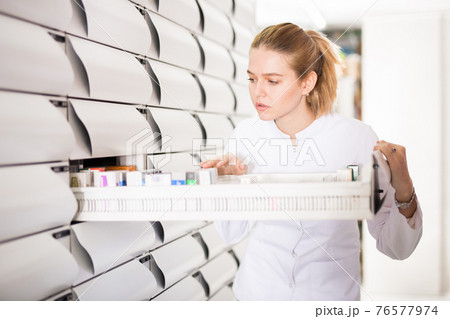 Young glad female customer searching for reliable drug in pharmacy Young glad female customer searching for reliable drug in pharmacy 76577974