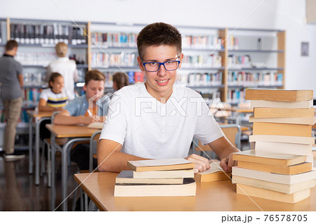 Schoolboy sitting with stacks of books in school library Schoolboy sitting with stacks of books in school library 76578705