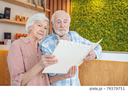 Gray-haired couple standing near reception in a spa center and looking trhough the price list Gray-haired couple standing near reception in a spa center and looking trhough the price list 76579751