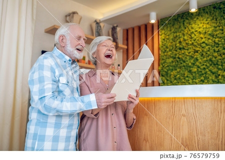 Gray-haired couple standing near reception in a spa center and laughing 76579759