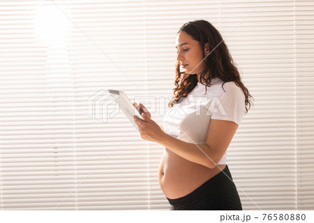 Happy pregnant young beautiful woman talking to her husband using video connection and tablet. Concept of communication and positive attitude during pregnancy 76580880