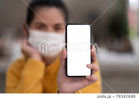 Mockup image of a beautiful woman wear mask while holding mobile phone with blank white screen. Mockup image of a beautiful woman wear mask while holding mobile phone with blank white screen. 76582686