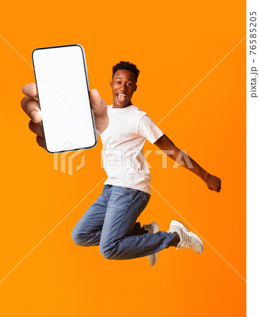 Overjoyed black man jumping and holding smartphone with white screen, mockup for advertisement or app design 76585205