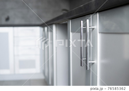 Modern minimalism style kitchen interior in monochrome tones. Custom kitchen with grey white facadesmdf and dark grey countertop with installed kitchen hood and sink. Modular kitchen from chipboard. 76585362