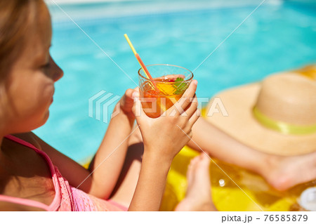 Little girl relaxing in swimming pool, enjoying suntans, drink a juice on inflatable yellow mattress Little girl relaxing in swimming pool, enjoying suntans, drink a juice on inflatable yellow mattress 76585879