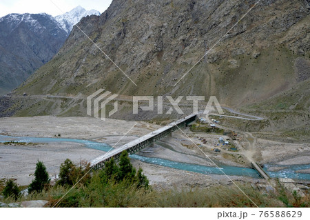A bridge over a turquoise river in the vast snow-capped mountains of the Himalayas 76588629