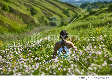 Young female sitting in green grass meadow in summer day 76589017
