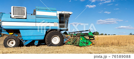 Scenic side view Big powerful industrial combine harvester machine reaping golden ripe wheat cereal field on bright summer or autumn day. Agricultural yellow field machinery landscape background 76589088