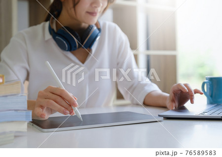 Fashion designer using tablet and sketches while working at table in studio. Fashion designer using tablet and sketches while working at table in studio. 76589583
