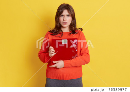 Frustrated woman with scale posing isolated over yellow background, lady being very upset and sad, female controlling her weight, has bad result, dresses casual clothing. Frustrated woman with scale posing isolated over yellow background, lady being very upset and sad, female controlling her weight, has bad result, dresses casual clothing. 76589977