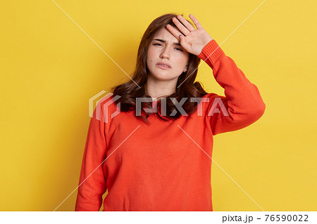 Tensed woman touching her head and looking directly at camera with tired painful look, dresses orange jumper isolated over yellow background, having problem with health. Tensed woman touching her head and looking directly at camera with tired painful look, dresses orange jumper isolated over yellow background, having problem with health. 76590022