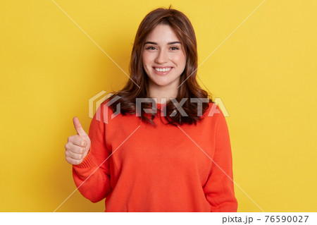 European happy young woman wearing orange clothes, holds finger up, shows like with thumb up isolated over yellow background, girl expressing positive, has satisfied look. European happy young woman wearing orange clothes, holds finger up, shows like with thumb up isolated over yellow background, girl expressing positive, has satisfied look. 76590027