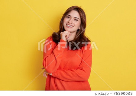 European charming girl with dark hair, holding fist under chin and smiling broadly, looking directly at camera, posing isolated over yellow background, expressing happiness. European charming girl with dark hair, holding fist under chin and smiling broadly, looking directly at camera, posing isolated over yellow background, expressing happiness. 76590035