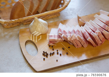 Studio shot of traditional Ukrainian food, tasty snack, slices of lard, garlic and peppercorn lying on cutting board, appetizer, having slices of bread in bread basket. People and traditions concept. Studio shot of traditional Ukrainian food, tasty snack, slices of lard, garlic and peppercorn lying on cutting board, appetizer, having slices of bread in bread basket. People and traditions concept. 76590676
