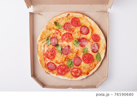 Top view of delicious hot pizza in box with ham and tomatoes sliced and served on white table, tasty supper for fast food lovers on light surface, box with pizza isolated over white background. Top view of delicious hot pizza in box with ham and tomatoes sliced and served on white table, tasty supper for fast food lovers on light surface, box with pizza isolated over white background. 76590680