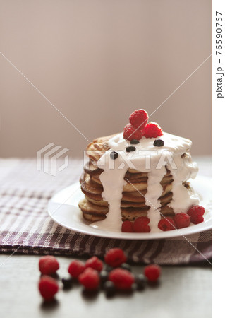 Photo of homemade pancakes with sour cream, raspberries and blueberries on white plate on cotton brown towel on wooden rustic table opposite concrete grey wall. Delicious breakfast in morning. 76590757