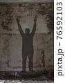 Shadow of a man with raised hands. 76592103
