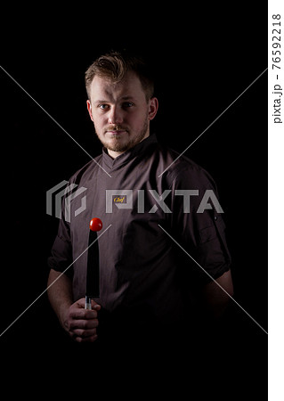 A chef in a uniform jacket shows off a professional chef's knife and a tomato 76592218
