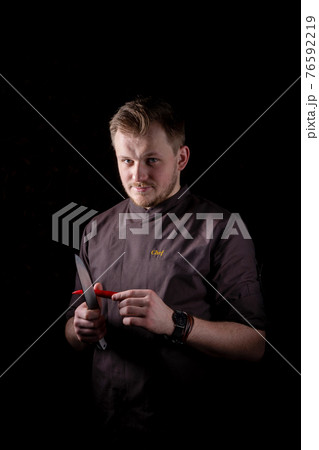 A chef in a uniform jacket cuts fresh red chili peppers with a chef's knife 76592219