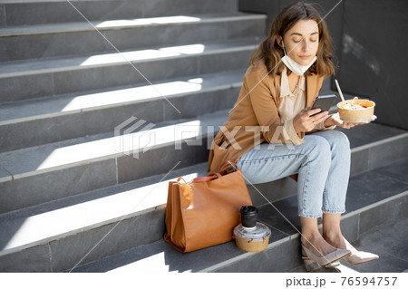 Woman have outdoor lunch on stairs near office building 76594757