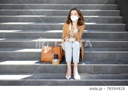 Woman have outdoor lunch on stairs near office building 76594828